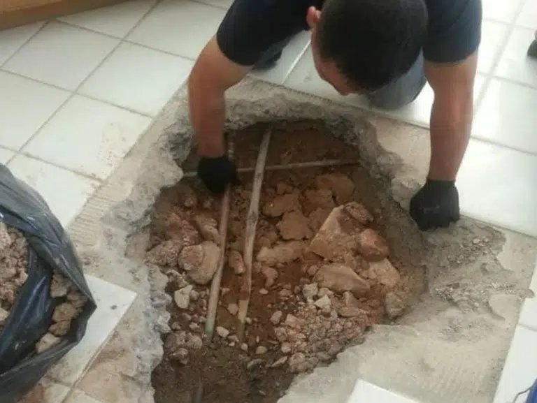 Technician digging through a tile floor and concrete slab to reach a leaking pipe